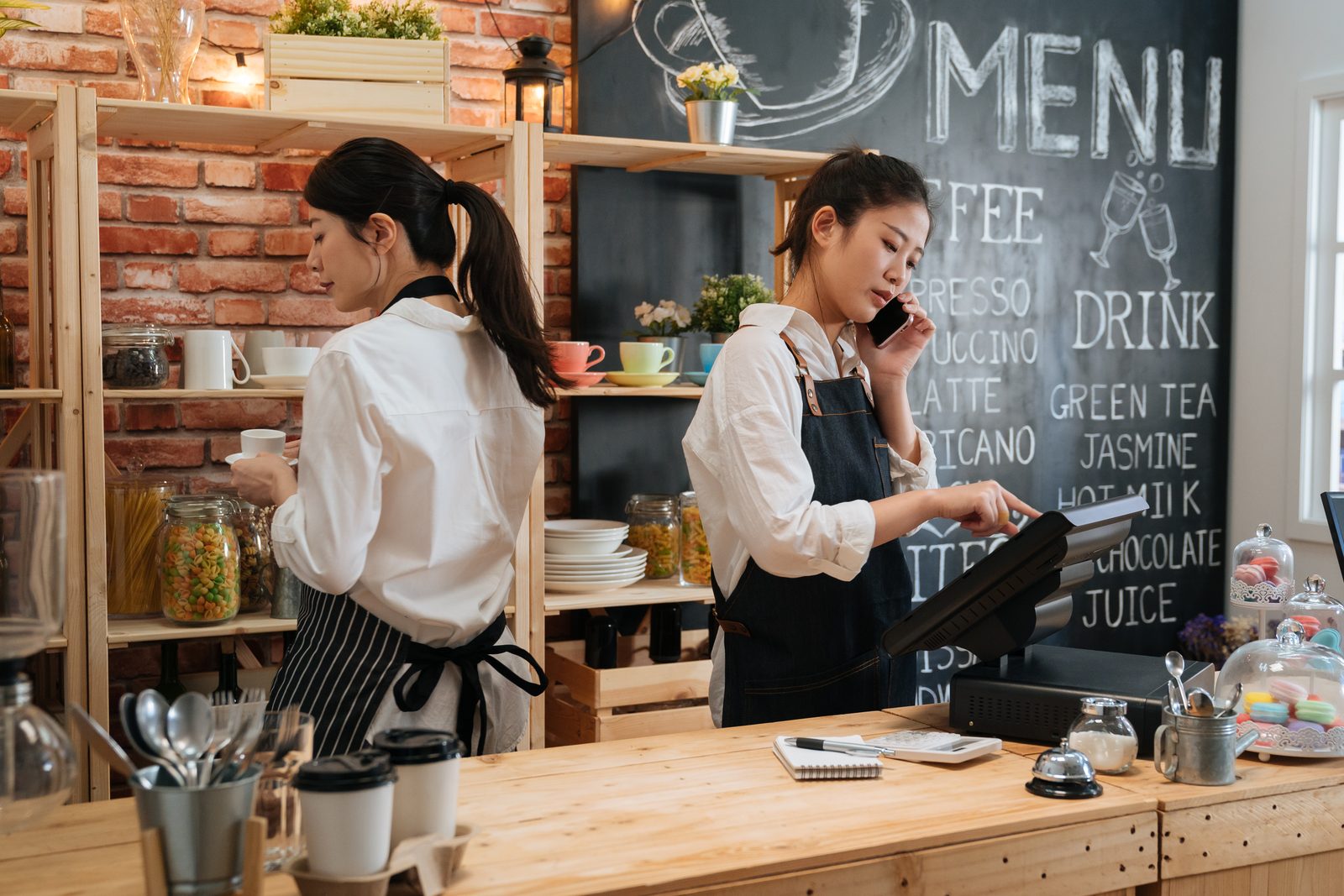 A café owner in an apron making coffee with her business partner behind the counter